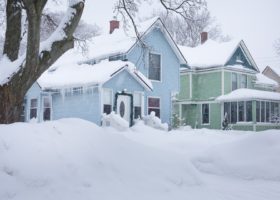 A blue and white house with a winter-ready roof is covered in snow.