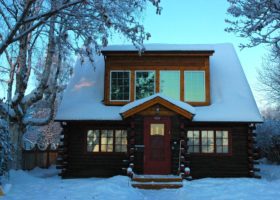 A small log cabin covered in snow, requiring immediate removal to ensure a safe roof.