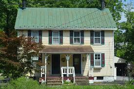 A yellow house with a green roof perfectly blends in the middle of a field, requiring occasional residential roofing maintenance.