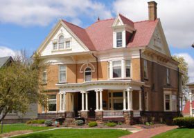 A tan house with a red roof that showcases the importance of proper roof maintenance.