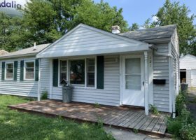 A small white house with a front porch in need of a roof inspection.