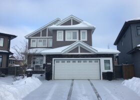 An energy-efficient house in the snow with a garage and driveway.