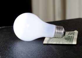 An energy efficient light bulb sitting on top of a dollar bill.