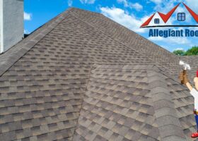 A man is standing on top of a shingled roof, inspecting a clogged gutter.