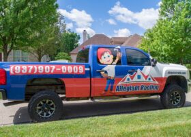 A blue and white truck parked in front of a house undergoing siding replacement.